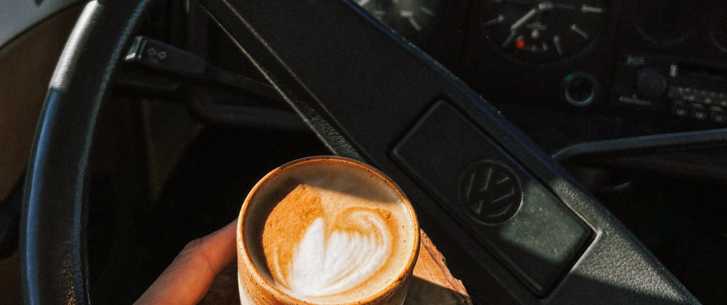 A cappuccino with a heart in the foam, held in front of the VW steering wheel