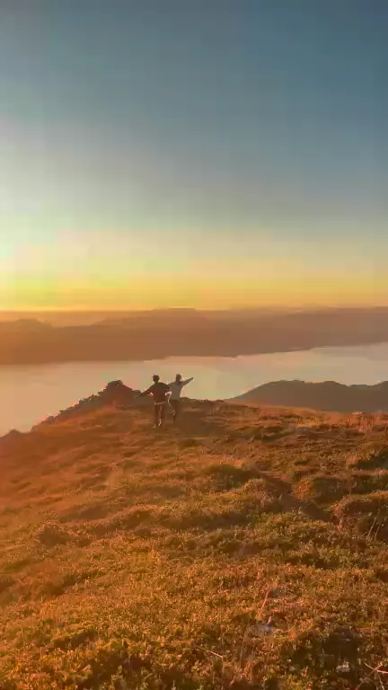 Two people sitting on a rock above the fjord at sunrise