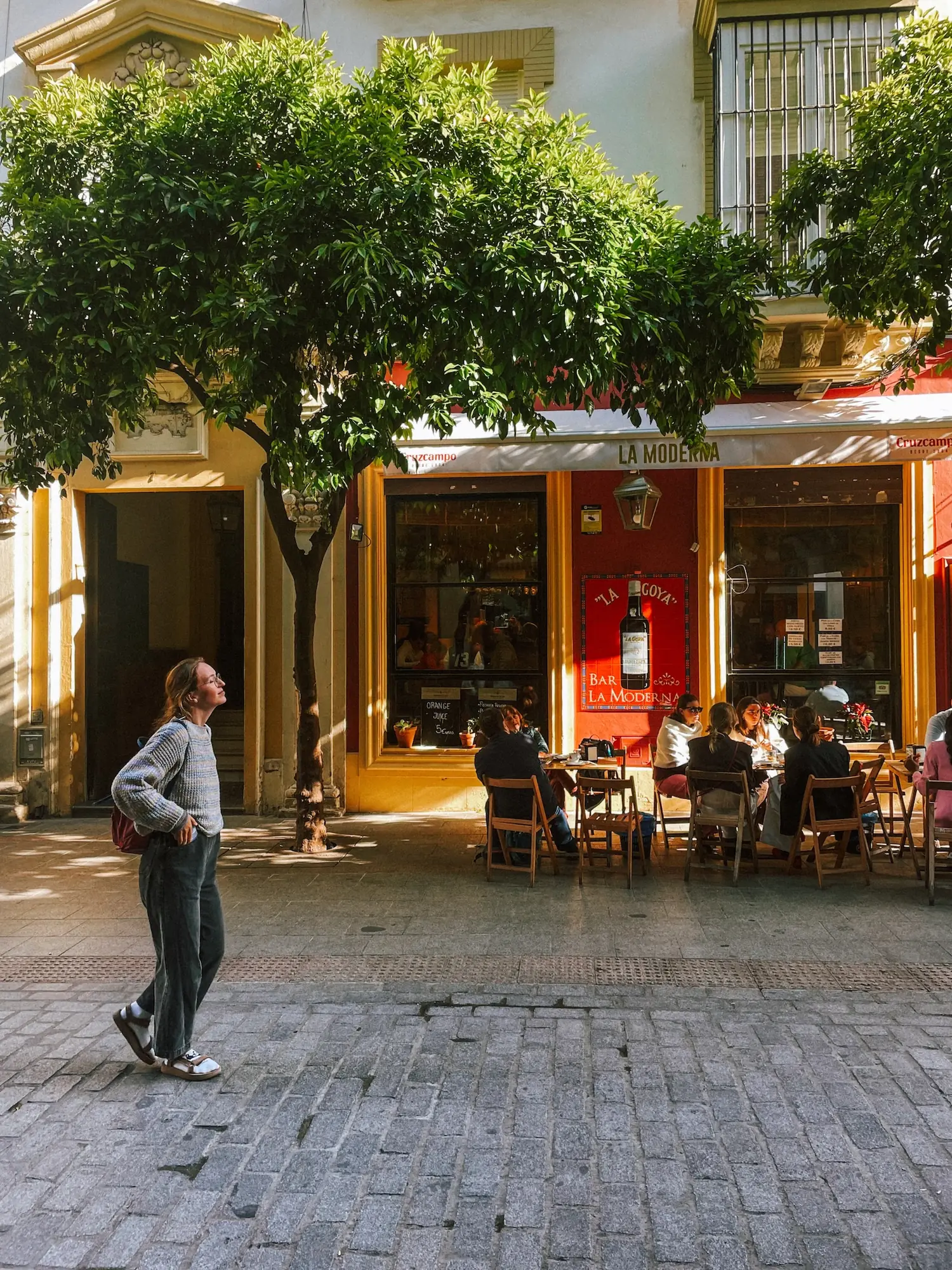a man walking past café terraces in the morning sun
