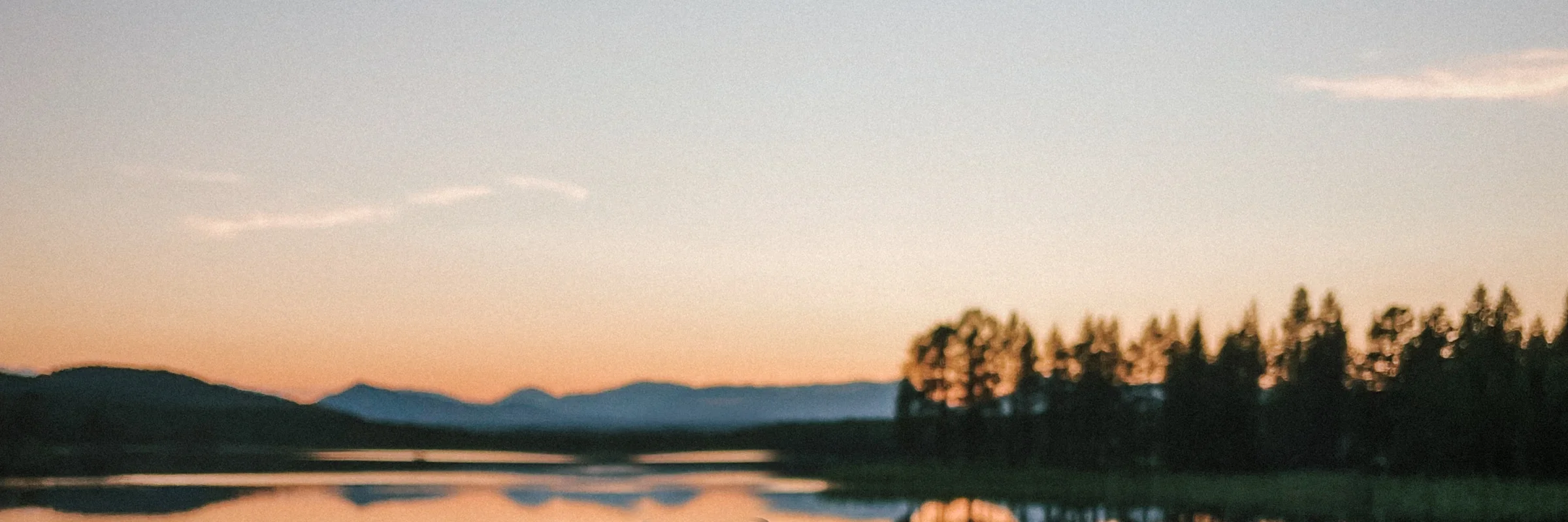 A still lake at dusk, with mountains and a treeline reflected in the water