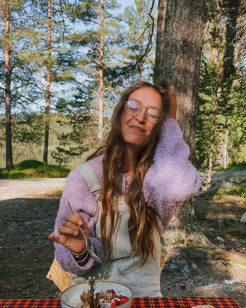 A guest smiling over a bowl and a cinnamon bun at a forest table